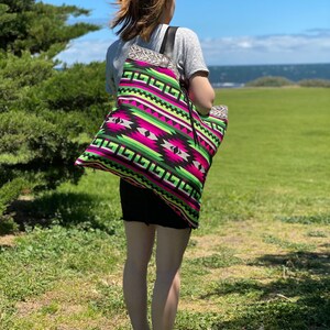 May include: A large tote bag with a colorful geometric pattern in shades of pink, green, black, and white. The bag has a black strap and is made of a woven fabric.