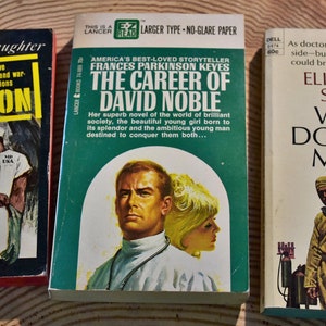 May include: Three vintage paperback books. The first, "Air Surgeon" by Frank G. Slaughter, features a doctor and woman on the cover. The second, "The Career of David Noble" by Frances Parkinson Keyes, has a man and woman. The third, "When Doctors Marry" by Elizabeth Seifert, shows two people.