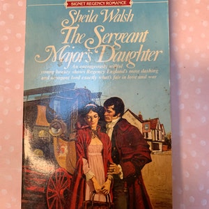 May include: A vintage paperback book titled "The Sergeant Major's Daughter" by Sheila Walsh. The cover features a romantic illustration of a woman in a red cloak and a man in a burgundy coat, with a carriage and buildings in the background. The book is a Signet Regency Romance.