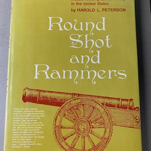 May include: A book cover with the title "Round Shot and Rammers" in large, ornate white lettering on a yellow background. The cover features a detailed illustration of a cannon in reddish-brown, with text describing the book's contents.
