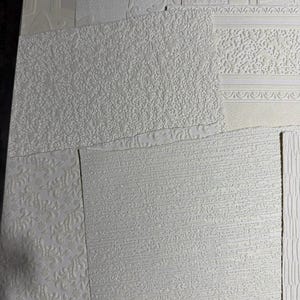 May include: Assortment of white textured wallpaper samples. The samples showcase various embossed patterns, including floral, brick, and linear designs. The textures range from subtle to pronounced, offering a variety of tactile experiences for interior design projects.