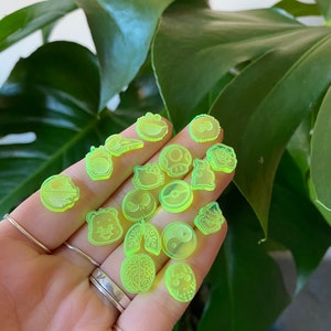 May include: A collection of 17 bright green acrylic charms featuring various cartoon and pop culture characters. The charms are small and feature detailed designs.