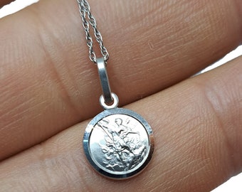 May include: Silver chain necklace with a round pendant featuring a detailed image of an angel with wings.