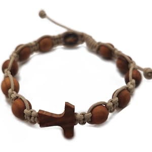May include: A handmade bracelet featuring wooden beads and a wooden cross. The beads are a warm brown color, strung on a beige cord. The cross is a darker shade of brown. The bracelet is adjustable.