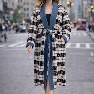 Può includere: Un cappotto lungo a quadri neri, bianchi e rossi, con colletto e cintura in denim. Il cappotto ha tasche e viene indossato con stivali neri. Il cappotto è un'elegante opzione di capospalla.