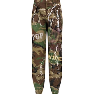 May include: Camouflage pants with white paint splatters and gold lettering that says "POP" and "ALL MY SELF".