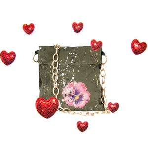 May include: A green canvas crossbody bag with a gold chain strap and a floral print. The bag has a flap closure and a small pocket on the front. The bag is surrounded by red heart-shaped embellishments.