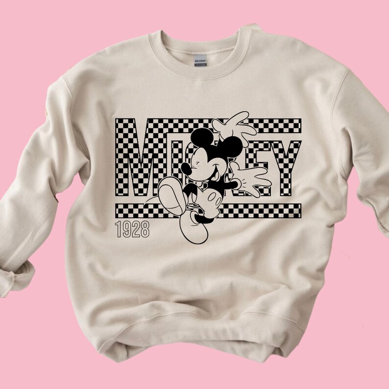 Puede incluir: Una sudadera beige con un dise&ntilde;o a cuadros en blanco y negro con Mickey Mouse y la palabra "MICKEY" con el a&ntilde;o "1928" impreso debajo.