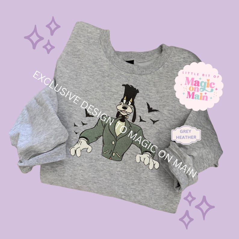 May include: A grey heather sweatshirt featuring a cartoon character dressed as a monster. The design includes a green jacket, white gloves, and black bats. Text on the sweatshirt reads "EXCLUSIVE DESIGN TO MAGIC ON MAIN" and "LITTLE BIT OF Magic on Main".