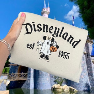 K&ouml;nnte beinhalten: Ein beiger Pullover mit einem schwarzen gestickten Design von Mickey Mouse, der als Geist verkleidet ist und einen K&uuml;rbis h&auml;lt. Der Text "Disneyland est 1955" ist ebenfalls auf dem Pullover gestickt.