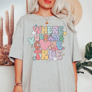 May include: Gray t-shirt with a colorful graphic that says "Where Dreams Come True" with Mickey Mouse ears, a castle, and stars.