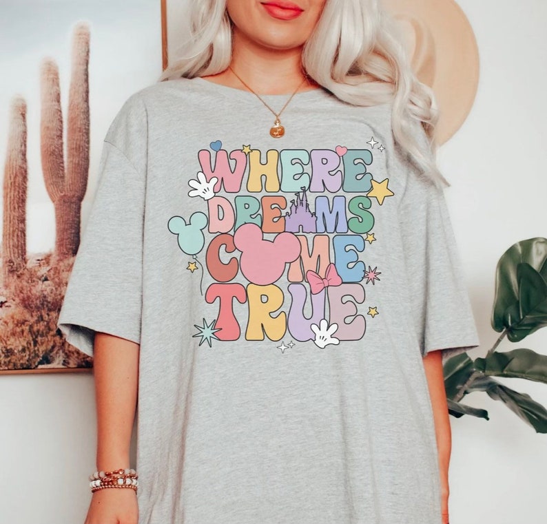 May include: Gray t-shirt with a colorful graphic that says "Where Dreams Come True" with Mickey Mouse ears, a castle, and stars.
