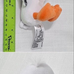 May include: White plush toy of a seagull with orange beak and feet. The seagull has black eyes with yellow stars in them. The toy is about 6 inches tall.
