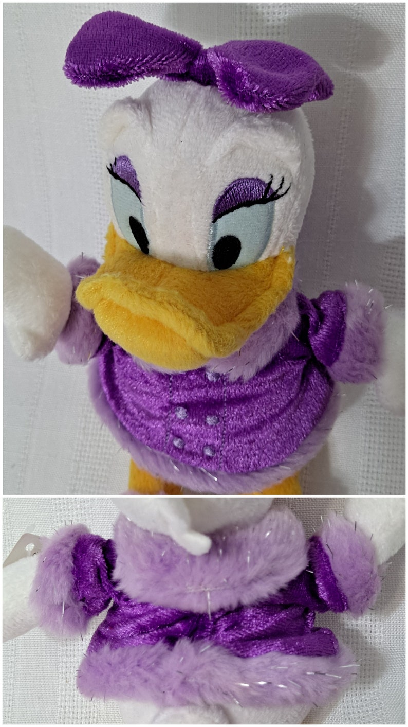 May include: A plush toy of Daisy Duck wearing a purple dress with a white fur trim and a purple bow in her hair.