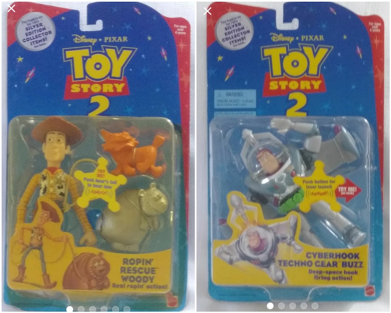 May include: Two Toy Story 2 action figures in their original packaging. The figures are Woody and Buzz Lightyear. Woody is wearing his classic cowboy outfit and is holding a lasso. Buzz Lightyear is wearing his space ranger suit and has a laser gun. The packaging is silver and blue and features the Toy Story 2 logo.