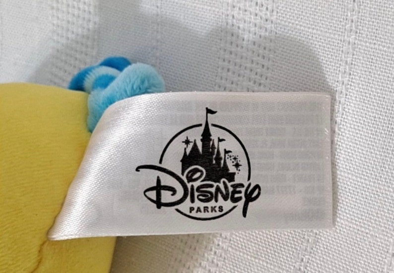 May include: A white tag with a black Disney Parks logo featuring a castle and the text "Disney Parks".