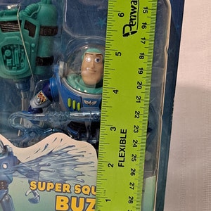 Peut inclure: Une figurine d'action en plastique bleu et vert de Buzz l'&Eacute;clair de la franchise Toy Story. La figurine tient un appareil qui projette de l'eau et se tient devant un fond bleu et blanc. L'emballage comprend le texte "Super Squirt Buzz" et "Squirt Evil to and Beyond".