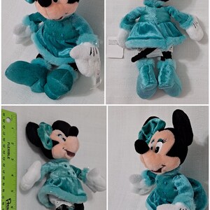 May include: A plush toy of Minnie Mouse wearing a teal blue dress with white fur trim and a matching teal blue bow. She is wearing white gloves and teal blue boots. The toy has a Disney Store tag attached to it.