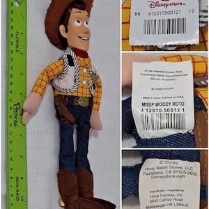May include: A plush toy of Woody from the Toy Story franchise. Woody is wearing his signature cowboy hat, vest, and jeans. The toy is approximately 12 inches tall. The toy has a Disney Store tag attached to it with the text "Disneystore. 412510500121 12 B8" and a barcode.