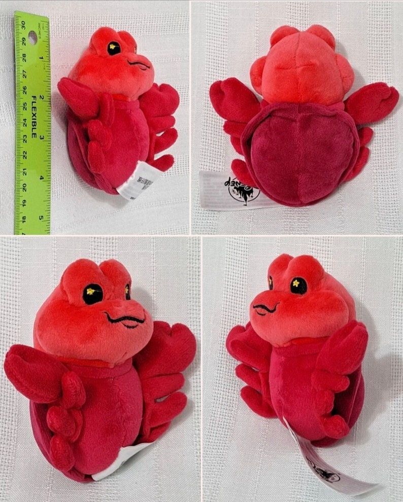 May include: A red plush crab toy with a Disney logo tag. The crab has large, black eyes and a smiling mouth.