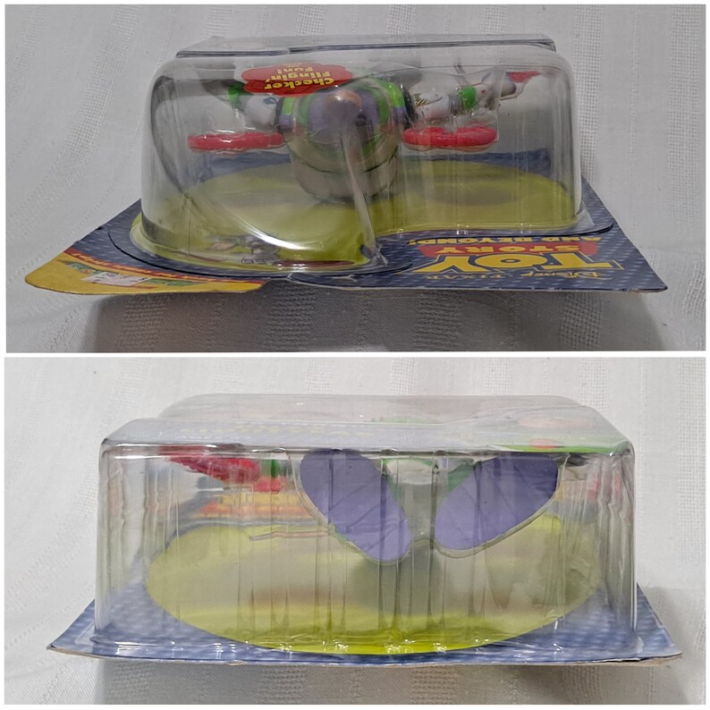 May include: A plastic packaging for a Buzz Lightyear toy from the Toy Story franchise. The toy is in a flying pose with red wings and a green and purple body. The packaging is clear and shows the toy in detail. The packaging has the Disney Pixar logo and the words "Toy Story" and "Buzz Lightyear" on it.
