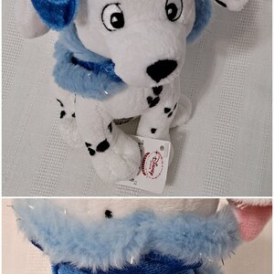 May include: A white and black Dalmatian plush toy wearing a blue bow and a blue fur collar. The toy has a Disney Store tag attached to it.