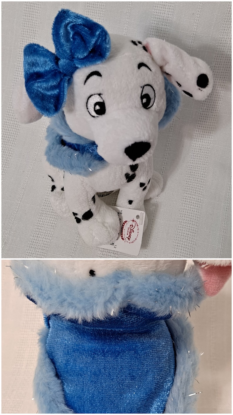 May include: A white and black Dalmatian plush toy wearing a blue bow and a blue fur collar. The toy has a Disney Store tag attached to it.