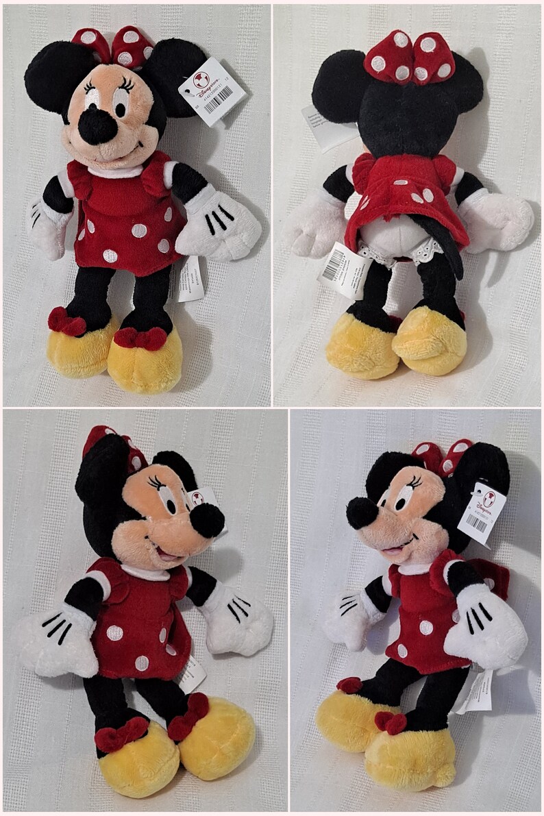 May include: A red and white polka dot dress with a red bow on top of the head. The plush toy is a black and white mouse with yellow shoes. The toy is wearing a white shirt with black cuffs. The toy is holding its hands up in the air. The toy is sitting on a white background.