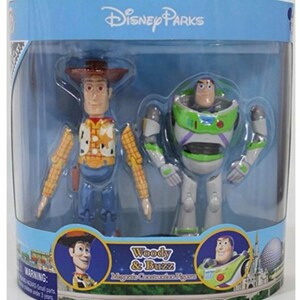May include: A set of two magnetic connection figures of Woody and Buzz Lightyear from the Toy Story franchise. The figures are packaged in a clear plastic box with a blue background and the text "Disney Parks" at the top. The figures are posed in a standing position and have a cartoonish appearance. The text "Woody & Buzz Magnetic Connection Figures" is printed on the bottom of the box.