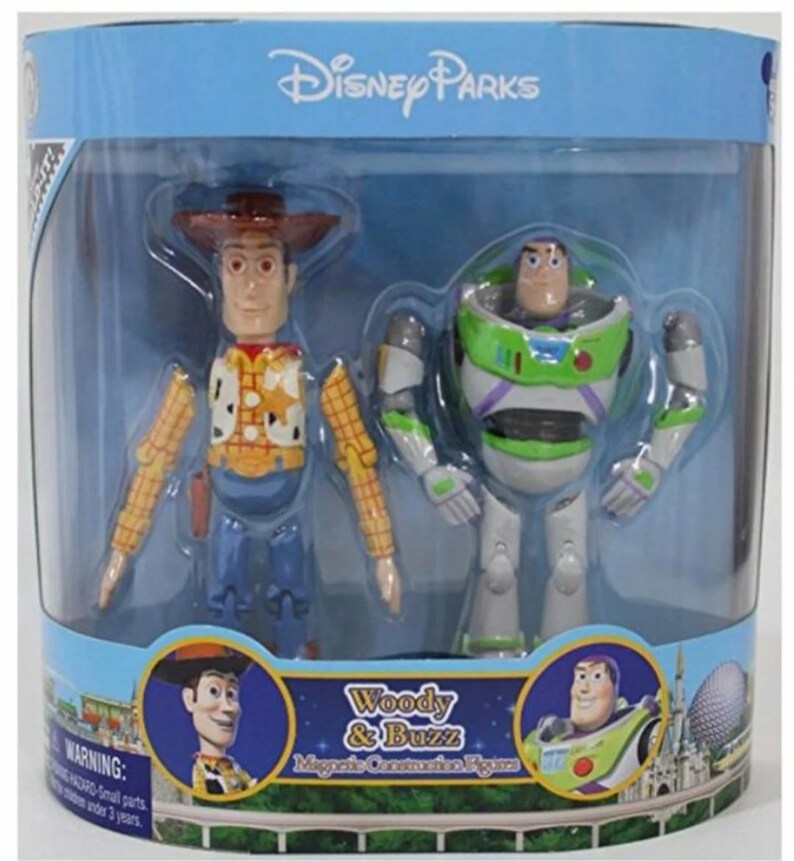 May include: A set of two magnetic connection figures of Woody and Buzz Lightyear from the Toy Story franchise. The figures are packaged in a clear plastic box with a blue background and the text "Disney Parks" at the top. The figures are posed in a standing position and have a cartoonish appearance. The text "Woody & Buzz Magnetic Connection Figures" is printed on the bottom of the box.