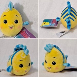 May include: Yellow and blue plush toy of a fish with a smiling face and a blue fin. The toy is about 5 inches tall and has a tag that says "Disney Parks Wish Upon A Star Adventure".