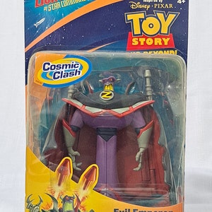 May include: A plastic action figure of the Evil Emperor Zurg from the Toy Story franchise. Zurg is wearing a purple cape and a black and gray suit with a red and gray chest piece. The figure is packaged in a plastic blister pack with a yellow and orange background. The packaging features the Toy Story logo and the words "Cosmic Clash" and "Rocket-Launchin' Evil Cape!"