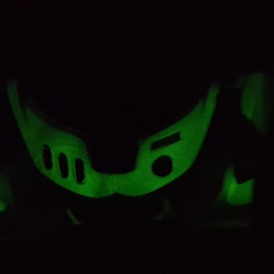 May include: A green glow-in-the-dark plastic toy in the shape of a helmet with three round holes on the front.