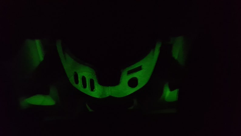 May include: A green glow-in-the-dark plastic toy in the shape of a helmet with three round holes on the front.