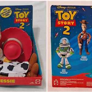 K&ouml;nnte beinhalten: Eine Pl&uuml;schpuppe von Jessie aus Toy Story 2, die einen roten Hut und ein Cowgirl-Outfit tr&auml;gt. Die Puppe sitzt auf einem blauen und gr&uuml;nen Karton mit dem Toy Story 2-Logo. Die Schachtel enth&auml;lt auch einen roten Hut und ein Paar braune Stiefel.
