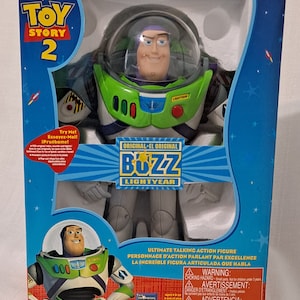 May include: A green and white Buzz Lightyear action figure from the Toy Story 2 movie. The figure is wearing a space ranger suit with a helmet and a red button that says "Lightyear". The figure is holding a laser gun. The box is blue and has a picture of Buzz Lightyear on it. The box says "Ultimate Talking Action Figure" and "Original - El Original Buzz Lightyear".