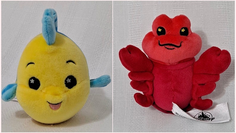 May include: Two plush toys, a yellow fish with blue fins and a red lobster. Both toys have big eyes with glitter accents and smiling mouths.