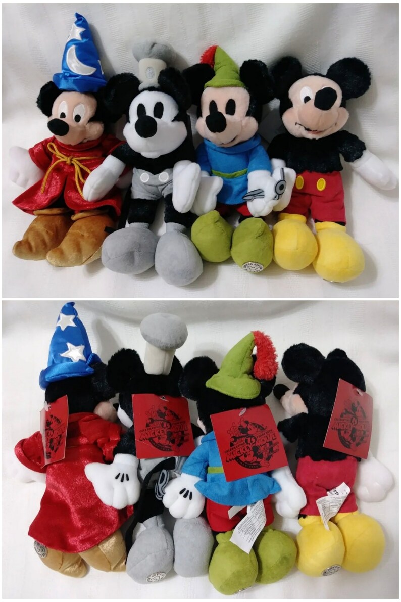 Op de afbeelding: Vier pluche Mickey Mouse-speelgoedjes gekleed in verschillende kostuums. De eerste is een tovenaar met een blauwe hoed en een rode mantel. De tweede is een Steamboat Willie met een zwart-witte outfit. De derde is een Robin Hood met een groene hoed en een blauw shirt. De vierde is een piraat met een zwart ooglapje en een rode broek. Alle vier speelgoedjes hebben een Mickey Mouse-label op hun rug met de tekst "Celebrating 90 Years of Mickey Mouse".