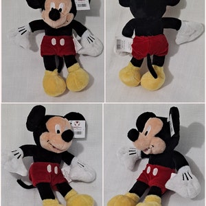May include: A plush Mickey Mouse toy with black fur, red shorts, and yellow shoes. The toy is sitting on a white surface.
