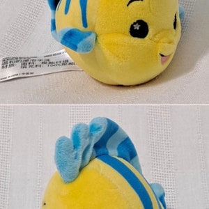 May include: A yellow and blue plush toy fish with a smiling face and a star on each eye. The fish has a blue fin and tail.