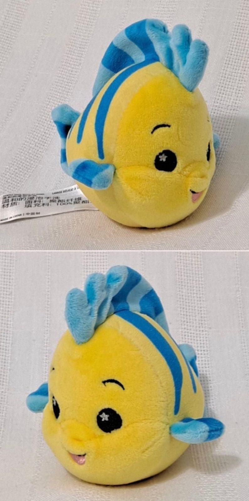 May include: A yellow and blue plush toy fish with a smiling face and a star on each eye. The fish has a blue fin and tail.