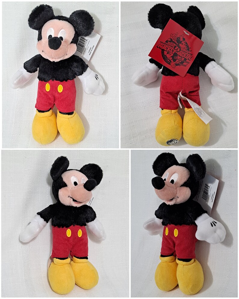 Op de afbeelding: Een zwart en rood pluche Mickey Mouse speelgoed met gele schoenen. Het speelgoed draagt een rood shirt met twee gele knopen en een zwarte broek. Het speelgoed heeft een label met de tekst "Celebrating 90 Years with Mickey Mouse".