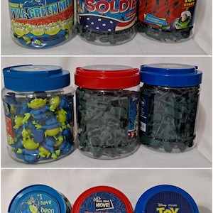 May include: Six clear plastic jars filled with various toy figures. The jars have blue and red lids with Toy Story themed labels. The labels include the text "Big Bucket O' Soldiers", "Little Green Men", "Toy Story", and "I have been chosen!"