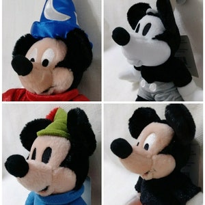Op de afbeelding: Vier pluche Mickey Mouse-speelgoed in verschillende kostuums. De eerste draagt een blauwe tovenaarshoed met een halve maan, de tweede draagt een zwart-wit Steamboat Willie-kostuum, de derde draagt een groene Robin Hood-hoed en de vierde draagt een zwart-rood Sorcerer Mickey-kostuum.