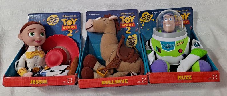 K&ouml;nnte beinhalten: Drei Pl&uuml;schtiere aus dem Disney Pixar Film Toy Story 2. Die Spielzeuge sind Jessie die Cowgirl, Bullseye das Pferd und Buzz Lightyear der Weltraum-Ranger. Jedes Spielzeug ist in einer bunten Schachtel mit dem Toy Story 2 Logo verpackt.