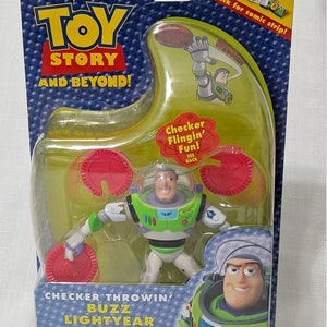 May include: Toy Story action figure of Buzz Lightyear in a green and white spacesuit, holding a red checker. The figure is packaged in a clear plastic box with a green and blue background. The box has the words "Checker Throwin' Buzz Lightyear" and "Ages 4+" printed on it.