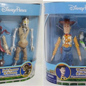 May include: Two sets of Disney Parks character figures. The first set features Jack Sparrow and a skeleton, both with posable limbs. The second set features Woody and Buzz Lightyear, also with posable limbs. Both sets are packaged in clear plastic boxes with blue backgrounds and the Disney Parks logo.