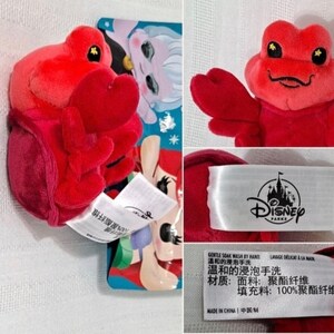 May include: Red plush crab toy with a smiling face and large, black eyes. The toy is approximately 4 inches tall and is labeled "Disney Parks".