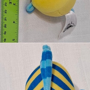 May include: Yellow and blue plush toy fish with a smiling face and a blue fin. The fish is about 5 inches long and has a white tag attached to it that says "Disney".
