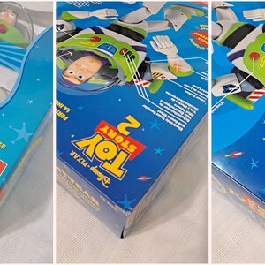 May include: A blue and white box with a picture of Buzz Lightyear from Toy Story 2. The box features the text "Buzz Lightyear" and "Toy Story 2".